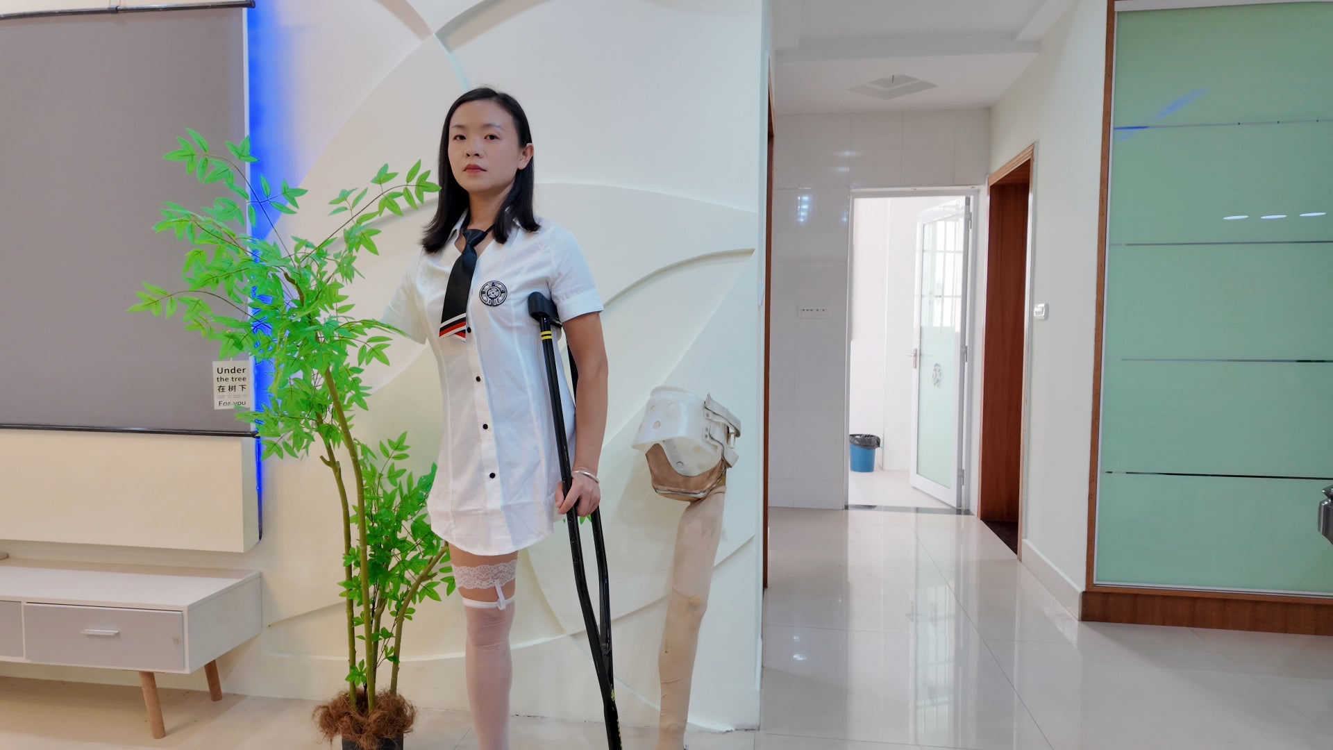 Mila: Ooe Amputee Girl - Walking indoors with crutches while wearing a white shirt and uniform.